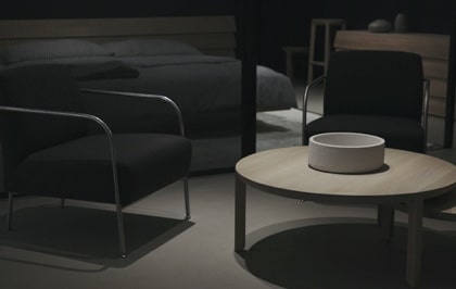 A cozy arrangement of dark furniture, featuring a round coffee table and a modern armchair in a dimly lit room.